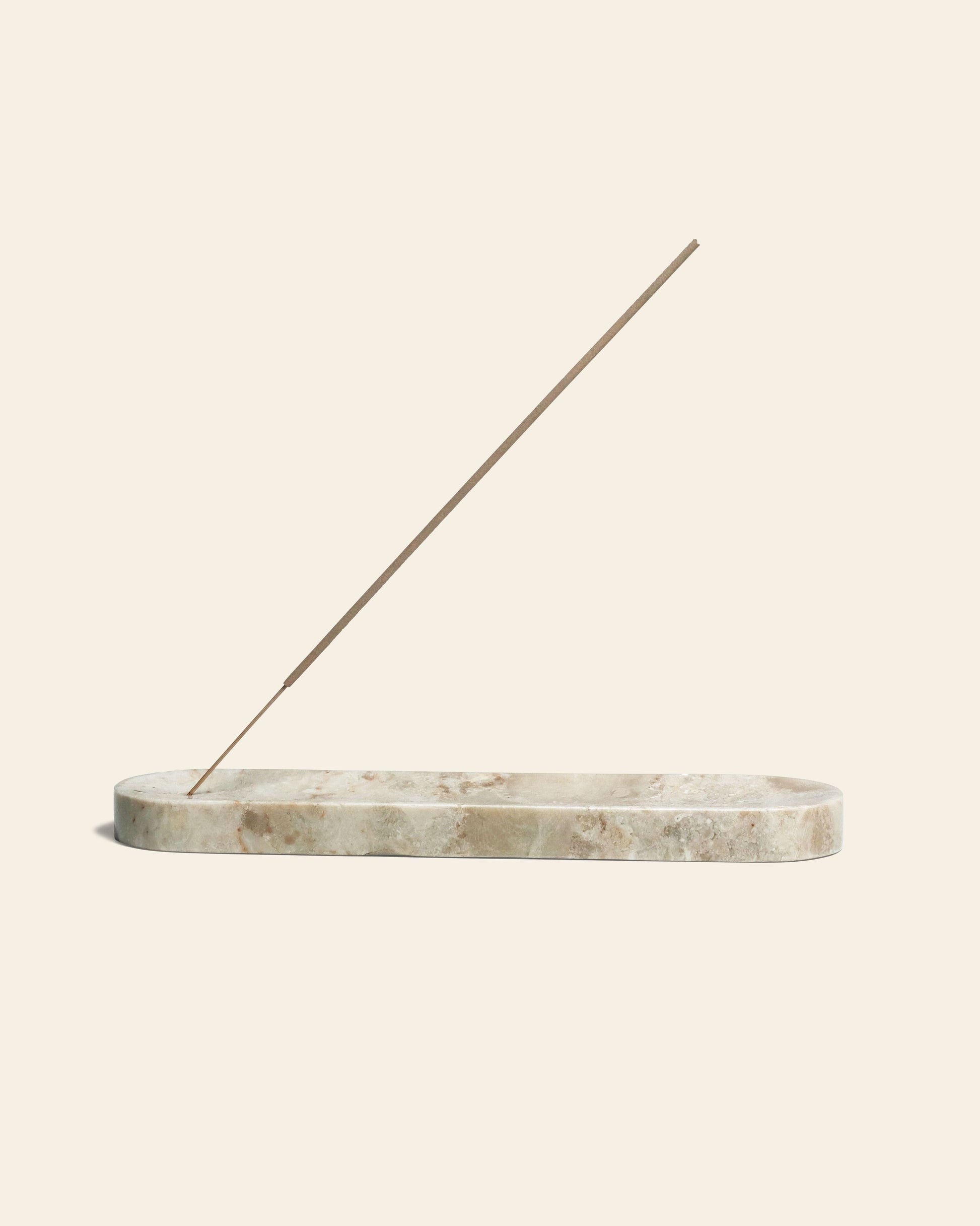 The stillgoods Horizon Incense Holder by stillgoods features an elongated marble design cradling a brown incense stick at a diagonal angle, set against a plain beige background—a versatile touch for any space.