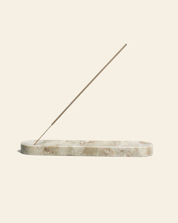 The stillgoods Horizon Incense Holder by stillgoods features an elongated marble design cradling a brown incense stick at a diagonal angle, set against a plain beige background—a versatile touch for any space.
