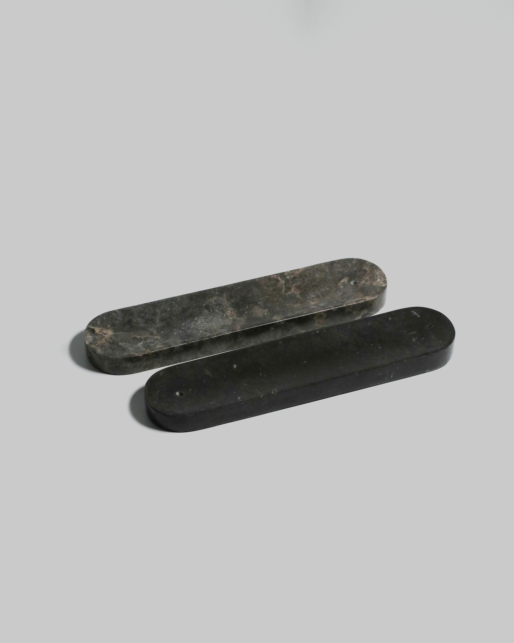 Two elongated, rounded black stillgoods Horizon Incense Holders with an elegant design are placed parallel on a light gray background, one slightly overlapping the other.