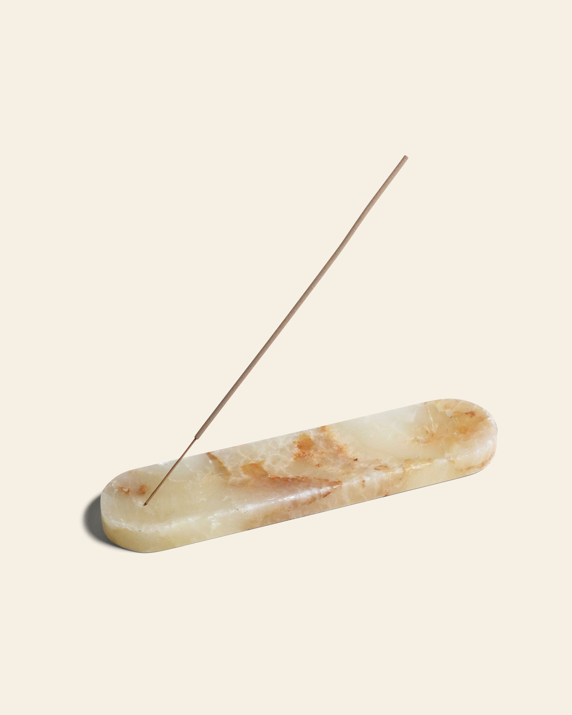 The stillgoods Horizon Incense Holder features a light-toned, elongated stone design with natural brownish patterns. It holds one lit incense stick at an angle, making it a versatile addition to any calm space.