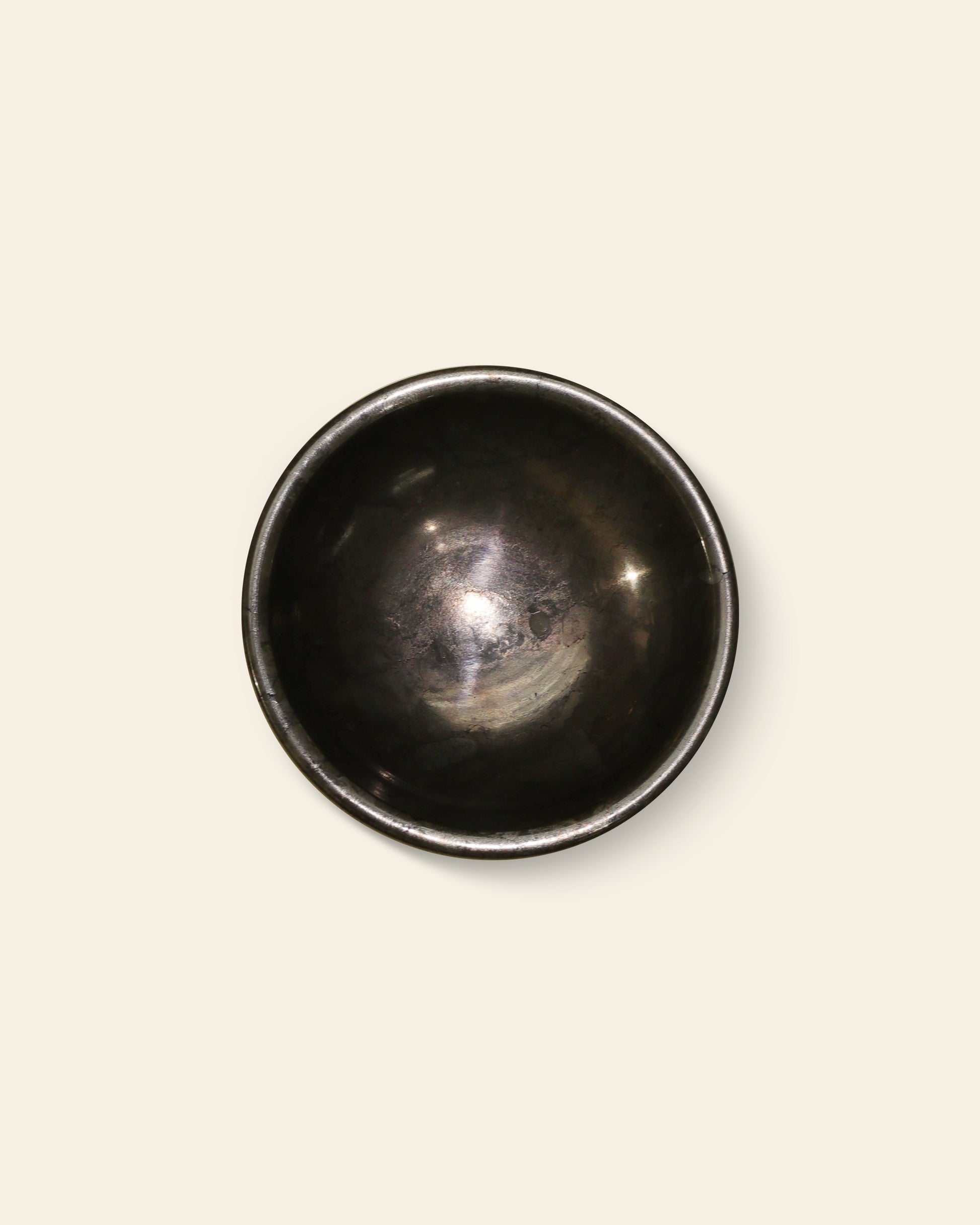 The stillgoods Luna Dish is a small, dark metal bowl with a smooth, rounded shape and a slightly reflective surface, photographed from above against a plain light beige background.