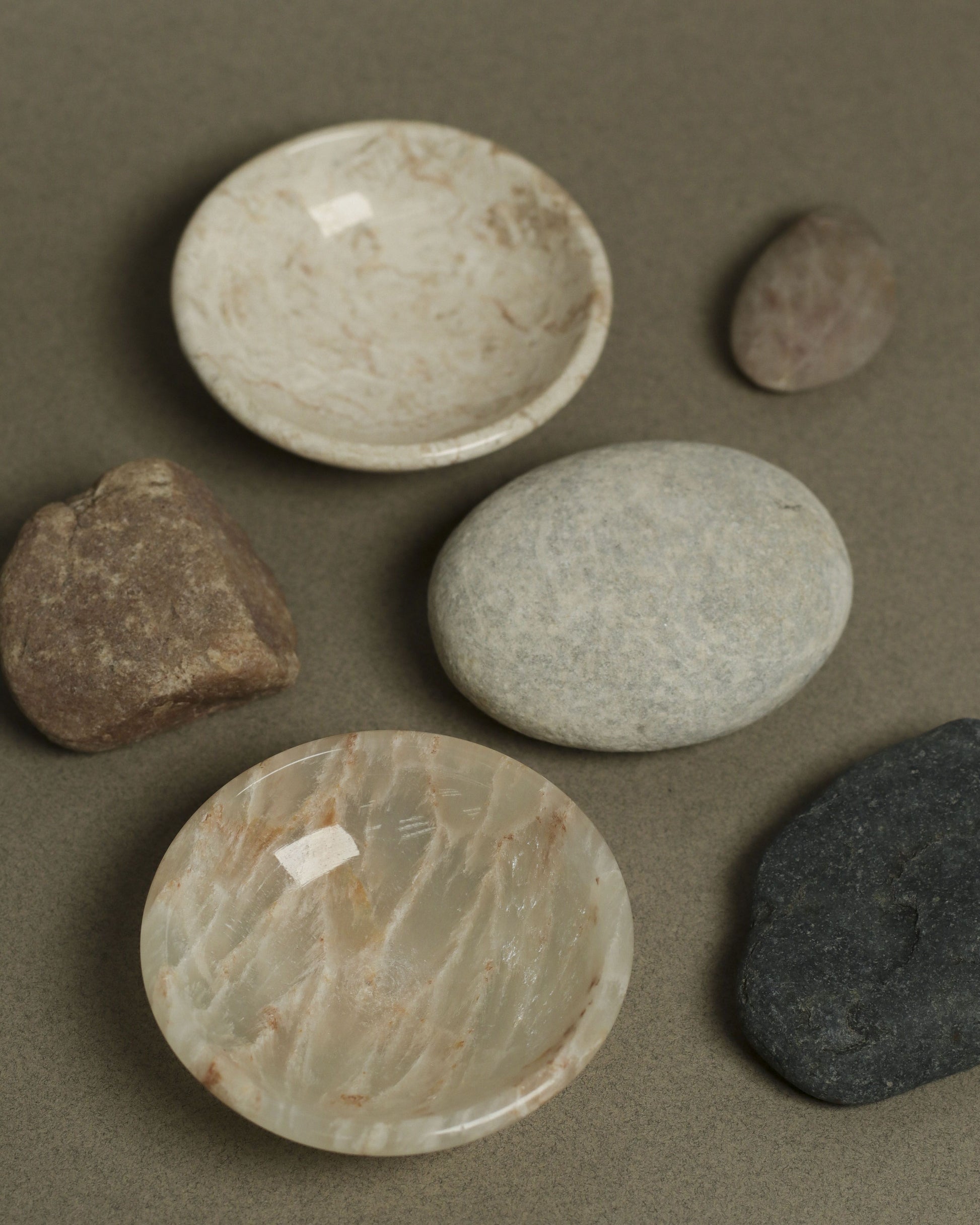 The stillgoods Luna Dish set features two round mini trinket dishes with a marbled design, placed on a neutral surface and surrounded by four smooth stones—ideal from stillgoods as stylish catch-all holders for your small treasures.