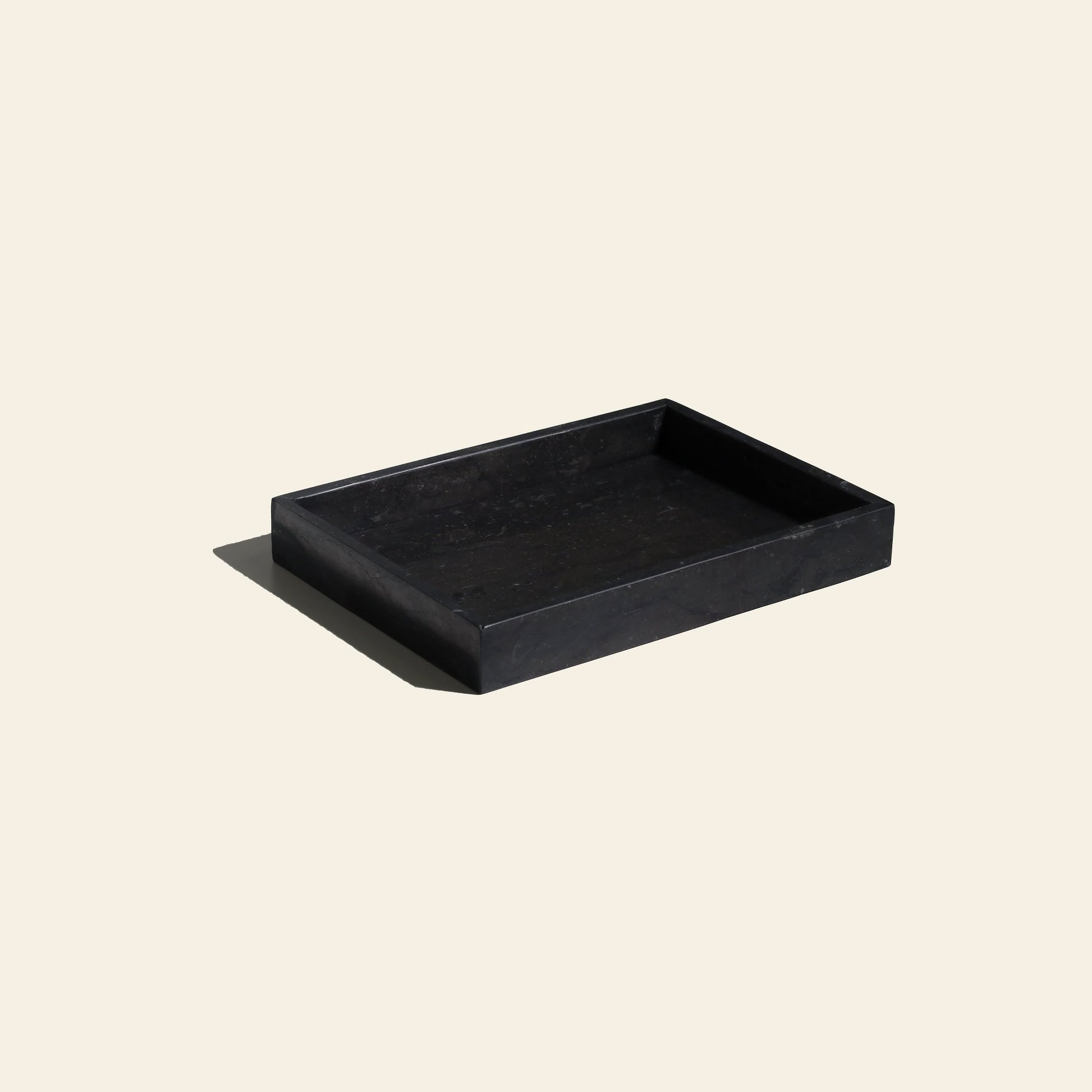 The stillgoods Mini Valor Tray, a rectangular black tray with raised edges and a low-profile design, sits elegantly on a light beige background. Its soft shadow highlights its depth—ideal for stylishly organizing your essentials.