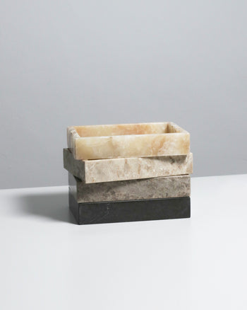 A stack of three stillgoods Mini Valor Trays in beige, light brown, and dark gray features a low-profile design, ideal for neatly organizing essentials on a white surface with a light gray backdrop.