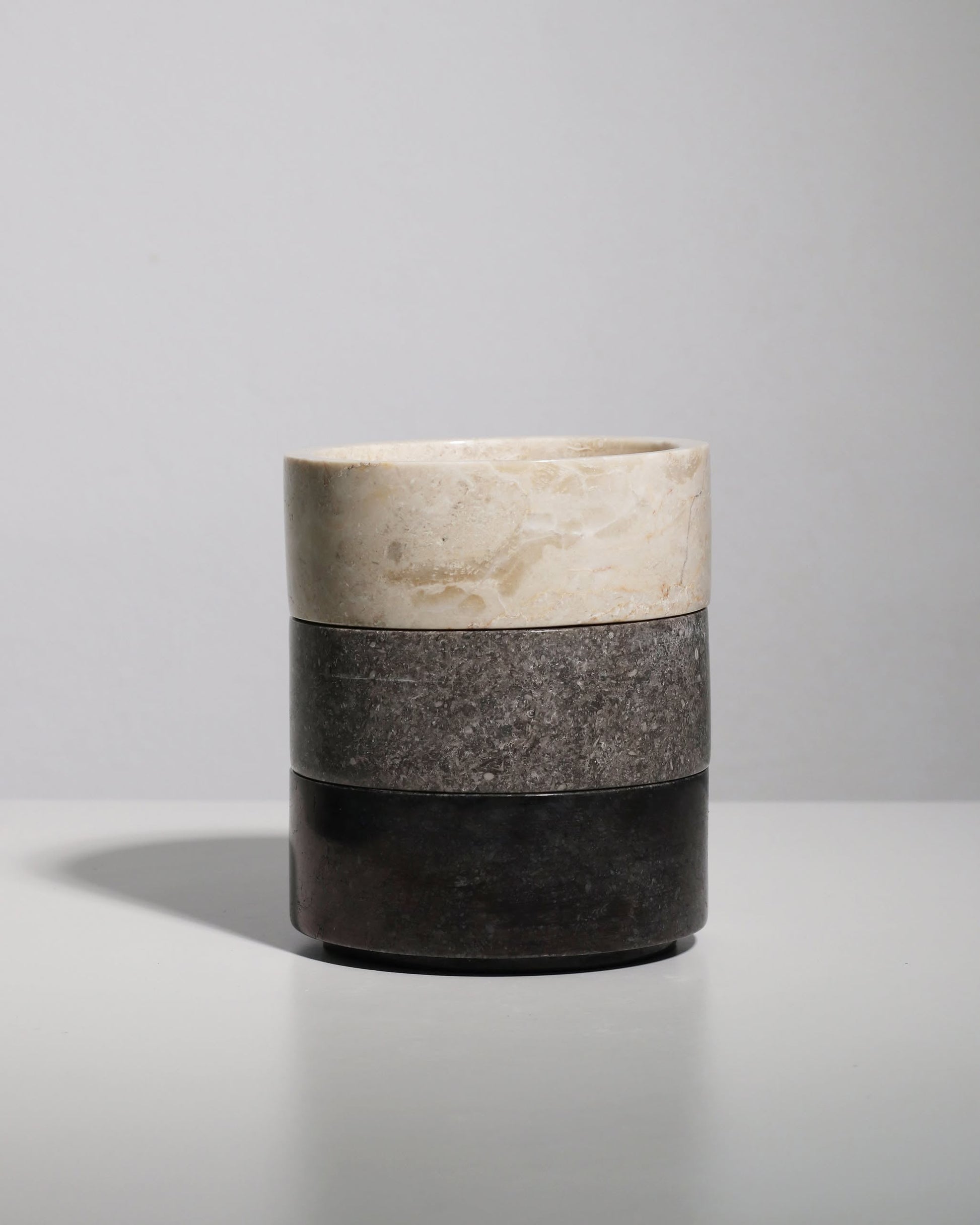The stillgoods Tingkat Bowl, a cylindrical bowl with three stacked sections in light beige, gray, and dark brown marble, is displayed on a white surface against a plain light gray background.