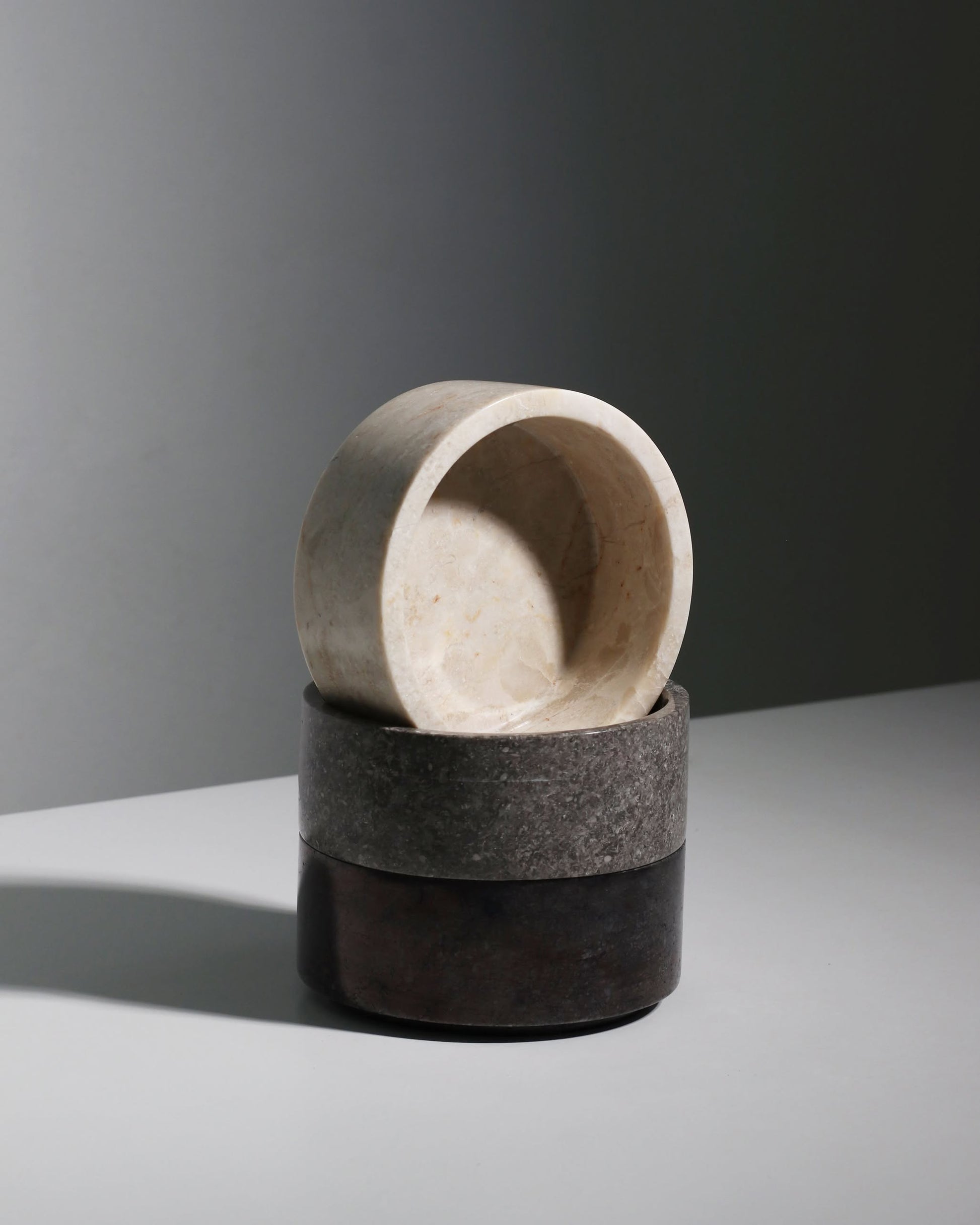 A stack of three stillgoods Tingkat Bowls in marble and onyx tones—beige, gray, and black—sits on a white surface against a softly lit plain background.